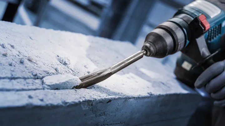 Person mit Sicherheitsausrüstung meißelt Beton mit einem Bohrhammer.