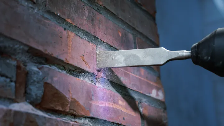 Meißelbohrer zum Entfernen von Mörtel zwischen Ziegeln an einer Wand.