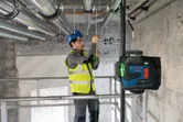 Eine Person in Schutzausrüstung richtet Rohre mithilfe eines Laser-Nivelliergeräts aus.