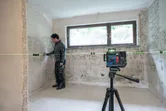 Eine Person, die Schutzausrüstung trägt, richtet mithilfe eines Laser-Nivelliergeräts Wandarmaturen in einem Raum aus.