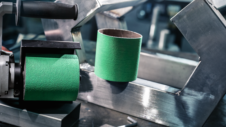 Grüne Schleifwalze neben einer passenden Schleifhülse auf einer Metallarbeitsfläche.