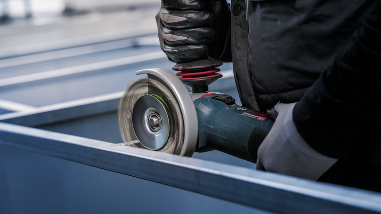 Eine Person mit Sicherheitsausrüstung verwendet einen Winkelschleifer, um einen Metallträger zu schneiden.