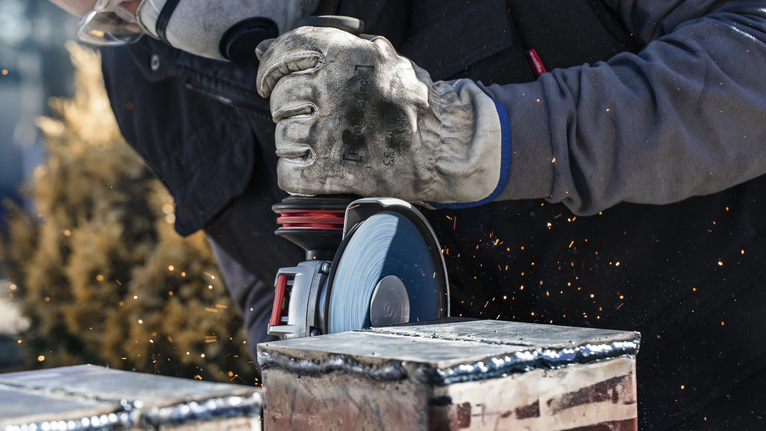 Eine Person mit Sicherheitsausrüstung schneidet mit einem Winkelschleifer Metall, wobei Funken fliegen.