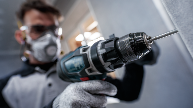 Arbeiter mit Sicherheitsausrüstung bohrt in eine Betonwand.