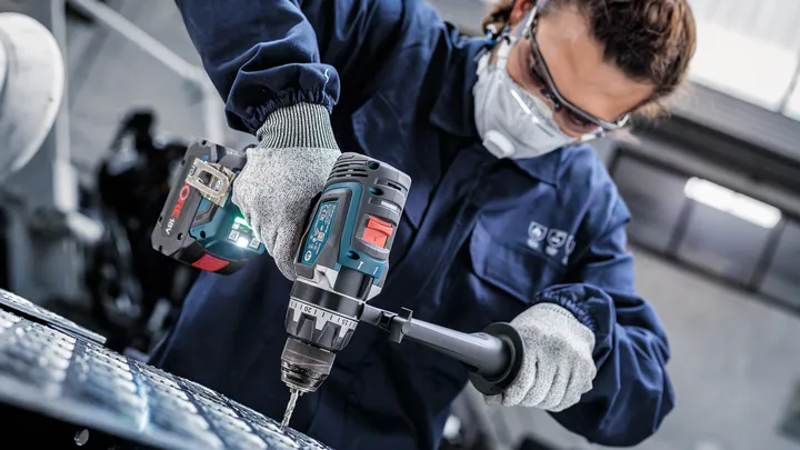 Eine Person mit Schutzausrüstung bohrt mit einem Akku-Elektrowerkzeug in Metall.