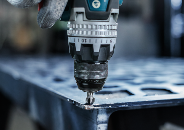 Eine Person mit Sicherheitsausrüstung bearbeitet ein Metallblech mit einer Bohrmaschine.