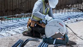 Eine Person mit Schutzausrüstung schneidet Stahlstangen mit einer Kreissäge, wobei Funken entstehen.