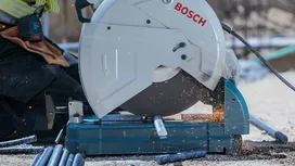 Eine Person mit Schutzausrüstung schneidet mit einer Kreissäge Metallstangen durch, wobei Funken entstehen.