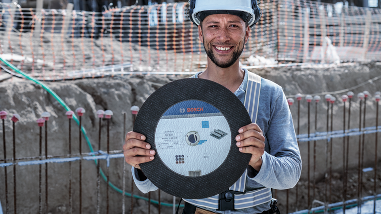 Eine Person mit Sicherheitsausrüstung hält auf einer Baustelle ein großes Kreissägeblatt.
