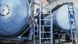 Eine Person mit Sicherheitsausrüstung schleift mit einem Elektrowerkzeug einen großen Metalltank.