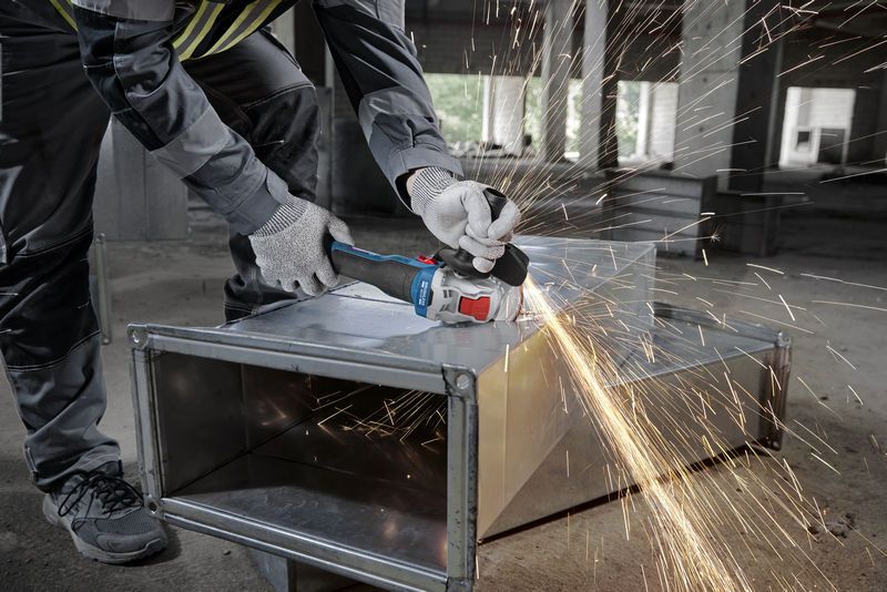Eine Person mit Schutzausrüstung schleift mit einem Winkelschleifer einen Metallkanal, wobei Funken entstehen.