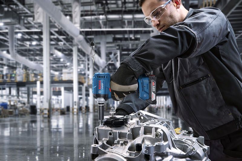Eine Person mit Schutzausrüstung bearbeitet mit einer Akku-Bohrmaschine ein Motorteil.