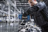 Eine Person mit Schutzausrüstung bearbeitet mit einer Akku-Bohrmaschine ein Motorteil.