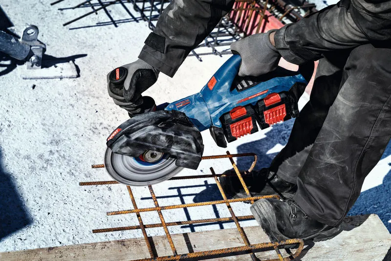 Eine Person mit Sicherheitsausrüstung schneidet auf einer Baustelle Bewehrungsstahl mit einem Akku-Winkelschleifer.