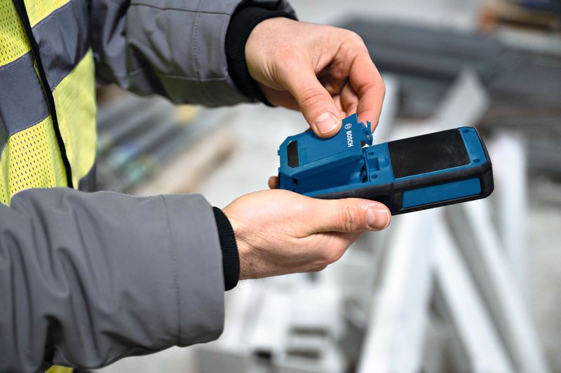 Eine Person mit Schutzausrüstung öffnet das Batteriefach eines Materialfeuchtemessgeräts.