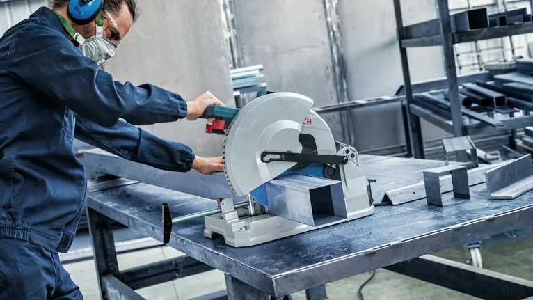 Eine Person mit Sicherheitsausrüstung schneidet in einer Werkstatt mit einer Kreissäge einen Metallträger.