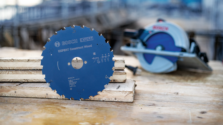 Ein Kreissägeblatt steht auf gestapeltem Holz neben einer Motorsäge auf einer Baustelle.