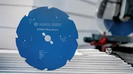 Blaues Kreissägeblatt auf gestapelten Faserzementplatten in einer Werkstatt.