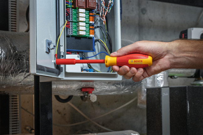 Eine Person benutzt einen isolierten Schraubendreher, um die Verkabelung im Inneren eines elektrischen Schaltschranks zu justieren.