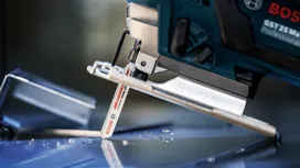 Eine Stichsäge schneidet durch eine Glasoberfläche mit verstreuten Glassplittern.