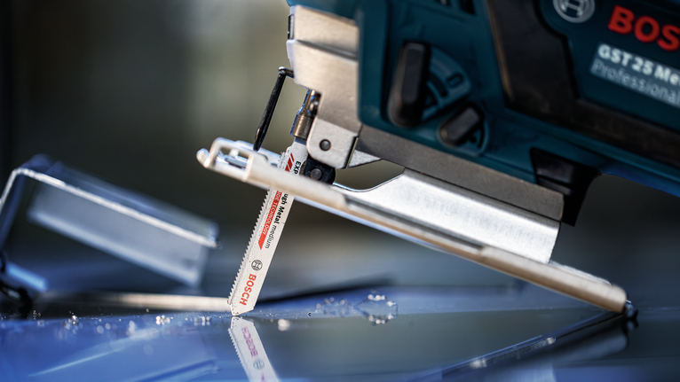 Eine Stichsäge schneidet durch eine Glasoberfläche mit verstreuten Glassplittern.