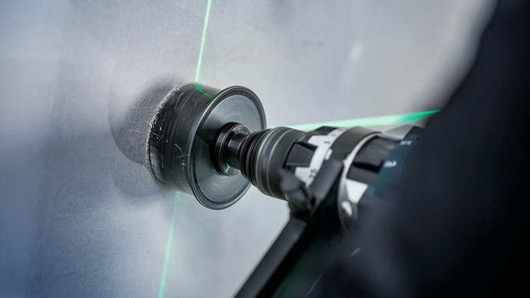 Eine Person, die Schutzausrüstung trägt, bohrt ein kreisrundes Loch in eine Betonwand.