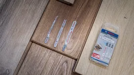 Drei Stichsägeblätter und ein Verpackungsset sind auf einem Laminatboden ausgestellt.