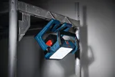 Kabellose Baustellenleuchte, montiert auf einem Metallgerüst, beleuchtet einen dunklen Arbeitsbereich.