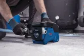 Eine Person in Schutzausrüstung schließt einen Schlauch an eine kompakte blaue Wasserpumpe an.