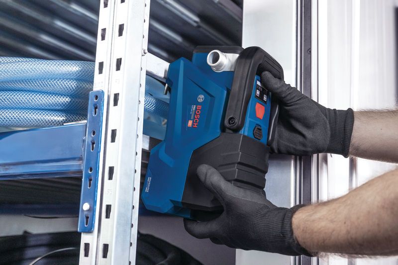 Eine Person in Schutzausrüstung installiert ein blaues Elektrowerkzeug in der Nähe von Metallregalen.