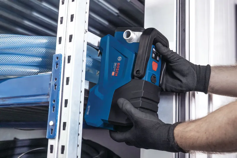 Eine Person in Schutzausrüstung installiert ein blaues Elektrowerkzeug in der Nähe von Metallregalen.