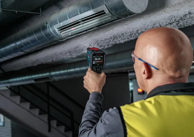 Eine Person, die Schutzausrüstung trägt, überprüft mit einem Thermodetektor einen Luftkanal.