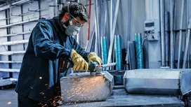 Eine Person, die Schutzausrüstung trägt, schleift eine Metallkiste und erzeugt dabei Funken.