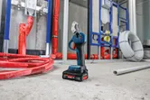 Die kabellose Rohrschere steht auf einer Baustelle, umgeben von Rohren und Sanitärmaterialien.
