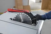 Eine Person in Schutzausrüstung wechselt das Sägeblatt einer Tischkreissäge.