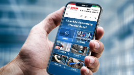 Eine Hand hält ein Smartphone mit der Bosch-Website und Werkzeugbildern.