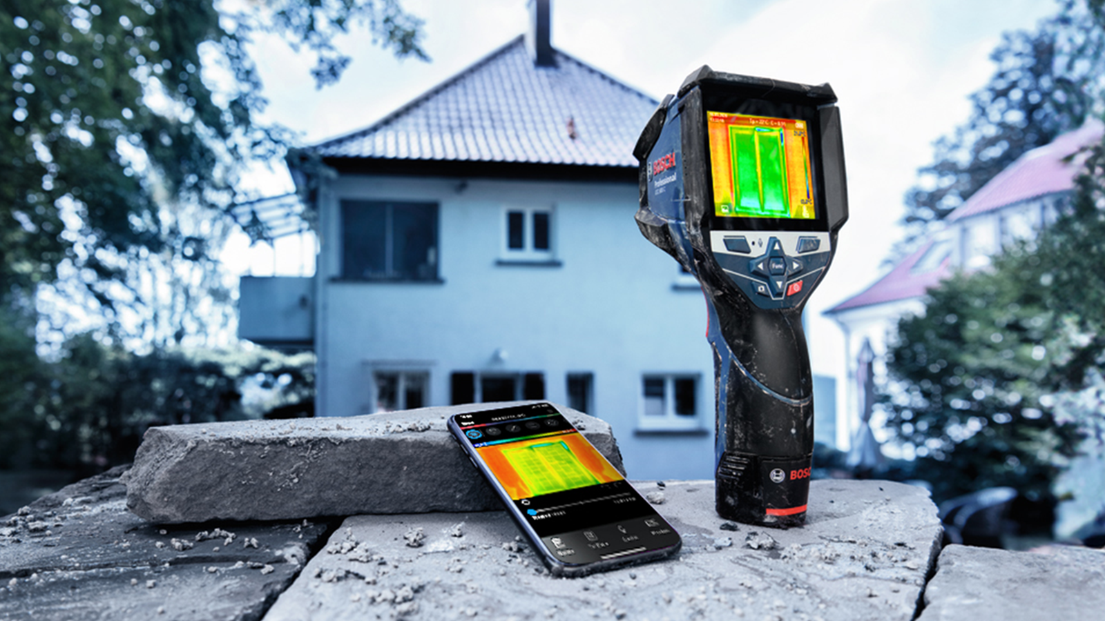 Bosch Professional Wärmebildkamera und Smartphone auf einem Stein, im Hintergrund ein Haus.