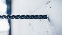 Ein metallischer Bohrer steckt in einer grauen Wand aus Beton.