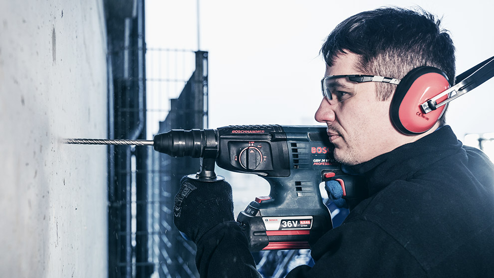 Ein Mann mit Gehörschutz bohrt mit einem Bosch Professional Akku-Bohrer in eine Wand.