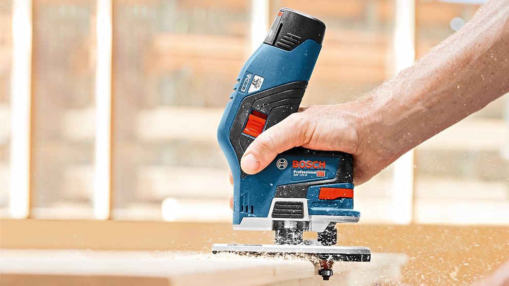 Eine Hand bedient eine blaue Bosch Professional Stichsäge, Holzspäne fliegen weg.