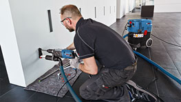 Ein Handwerker kniet mit einem Bosch Professional Werkzeug vor einer Wand.