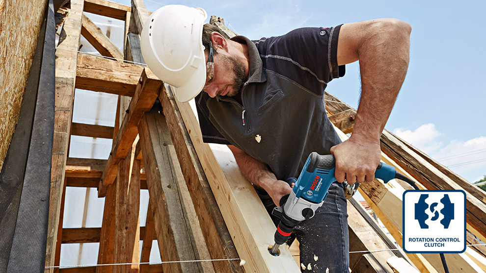 Ein Handwerker mit Helm bohrt in Holz mit einem blauen Bosch Professional Werkzeug.