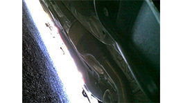 Ein Blick unter ein Fahrzeug auf eine glänzende Motorhaube und den Asphalt.