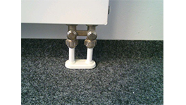 Weiße Heizkörperfüße mit Metallventilen auf grauem Teppichboden.