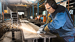 Ein Mann mit Gehörschutz schleift Metall in einer hellen Werkstatt.