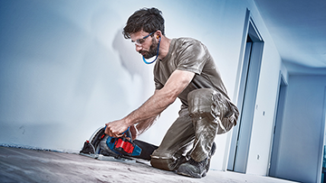 Mann kneelt und schneidet mit einer Bosch Professional Maschine den Boden.