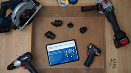 Bosch Professional Werkzeuge und Tablet auf Holzoberfläche, umgeben von Zubehörteilen.