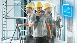 Mann mit Helm und Smartphone in Baustellenumgebung, mit Messtechnik.