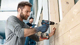 Mann mit Bosch Professional Akku-Bohrschrauber befestigt Holzplatten an einer Wand.