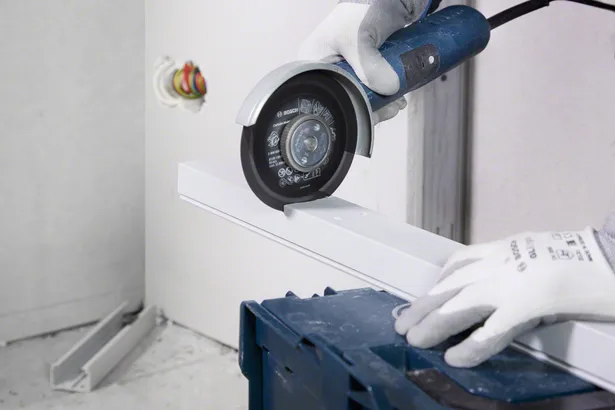 En arbejder iført sikkerhedsudstyr skærer en metalkanal med en vinkelsliber.